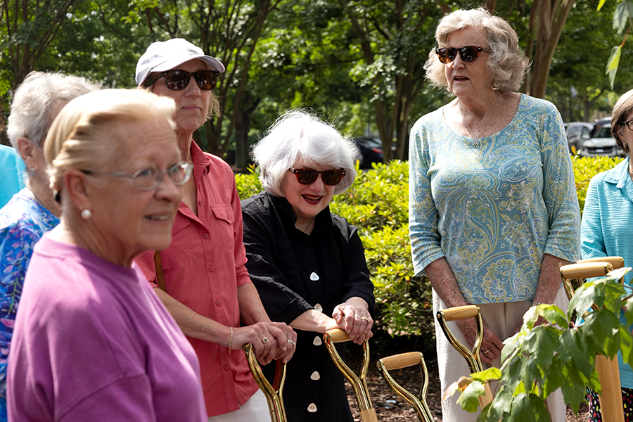 A group of women gather around a young tree they will plant on a college campus.