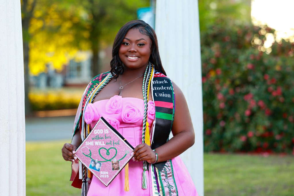 A woman with graduation cords over her shoulders smiles for a photo.,