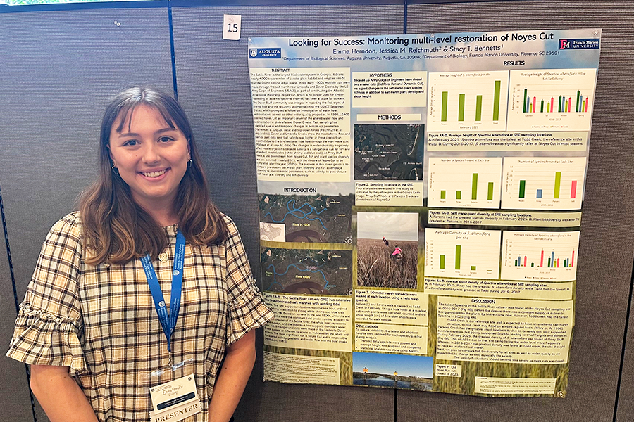A college woman stands next to a scientific poster. Her project is titled, "Looking for Success: Monitoring multi-level restoration of Noyes Cut."
