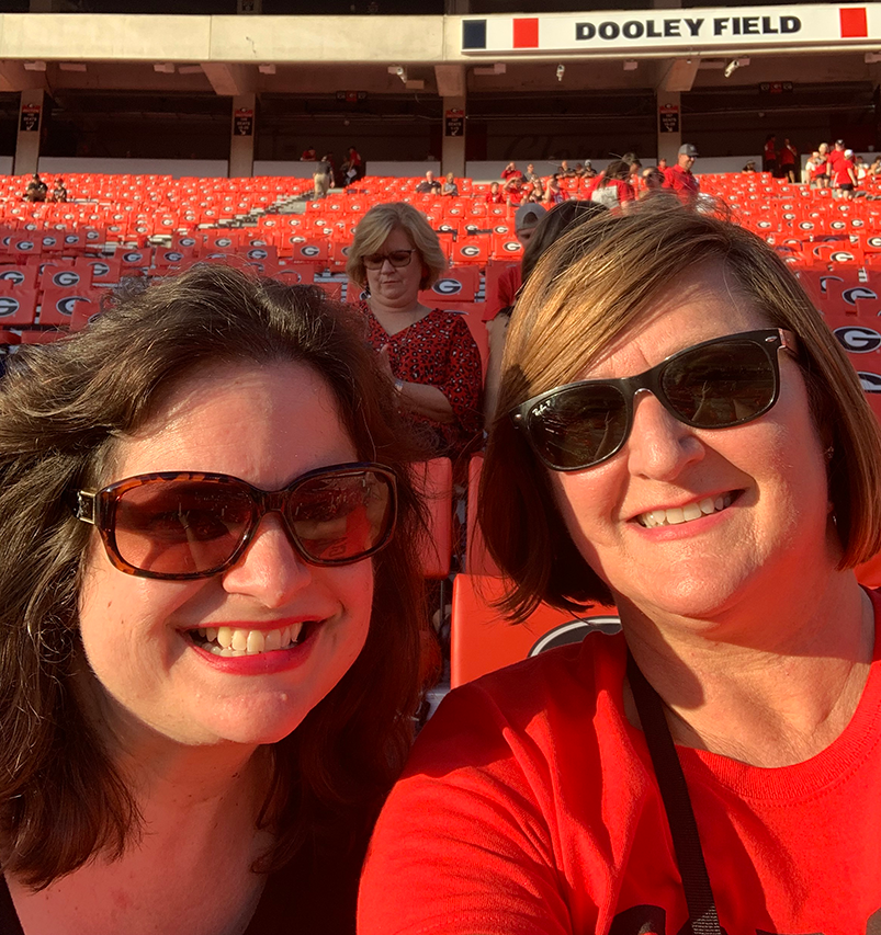 Two smiling women wearing sunglasses take a selfie at Sanford Stadium.