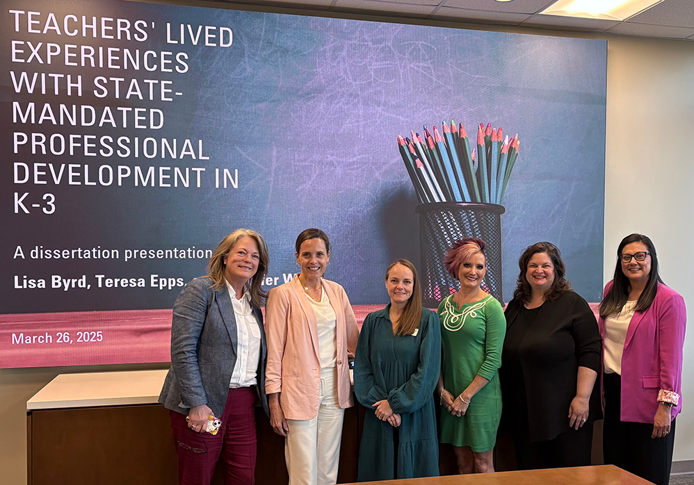 Six well-dressed women smile for the camera at a dissertation presentation.