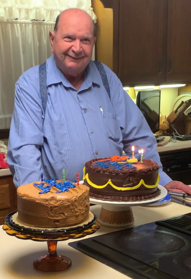 A smiling man stands behind two birthday cakes.