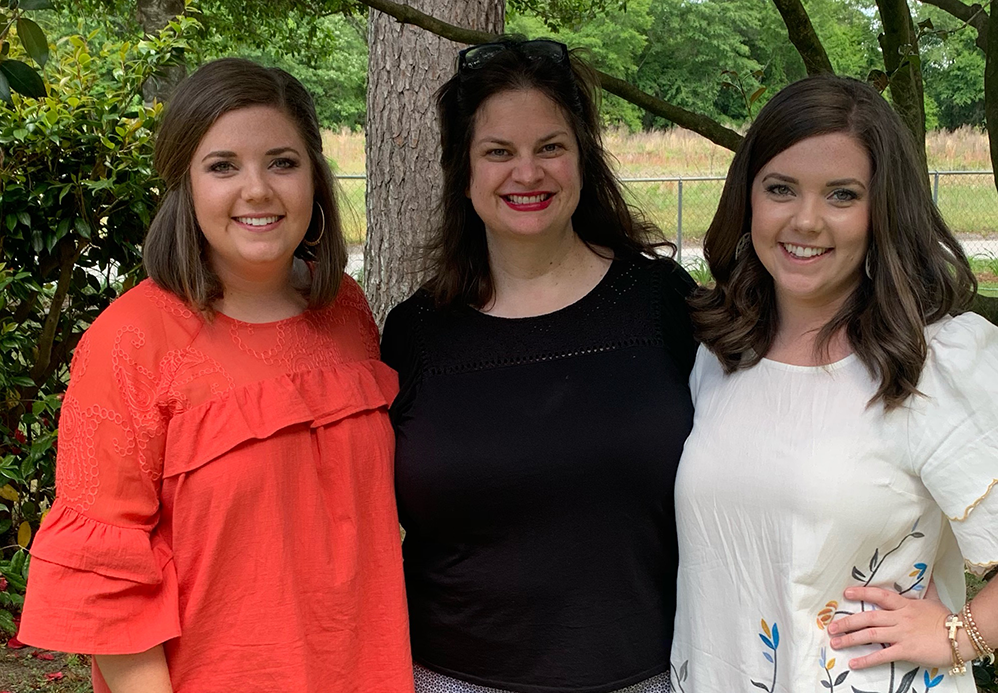 Three women standing outside and smiling at the camera.