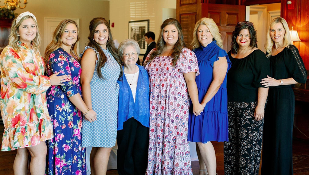 Eight well-dressed woman stand in a line and smile at the camera.