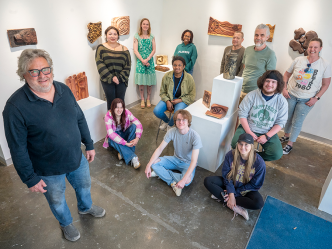 Men and women, some seated, some standing in a small room with wooden projects on the wall and around them.