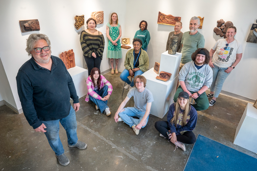 Men and women, some seated, some standing in a small room with wooden projects on the wall and around them.