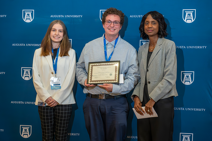 A male college student accepts an award presented by two women.