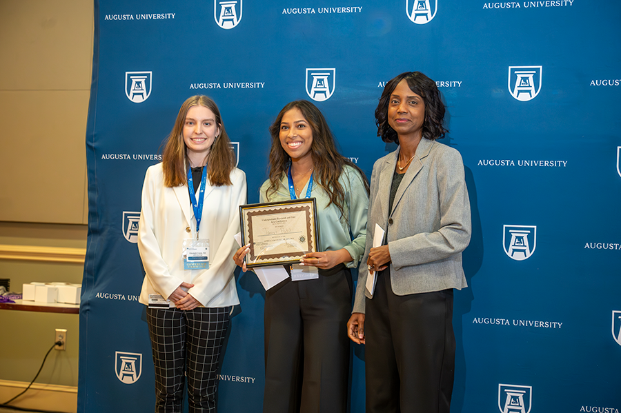 A female college student accepts an award presented by two women.