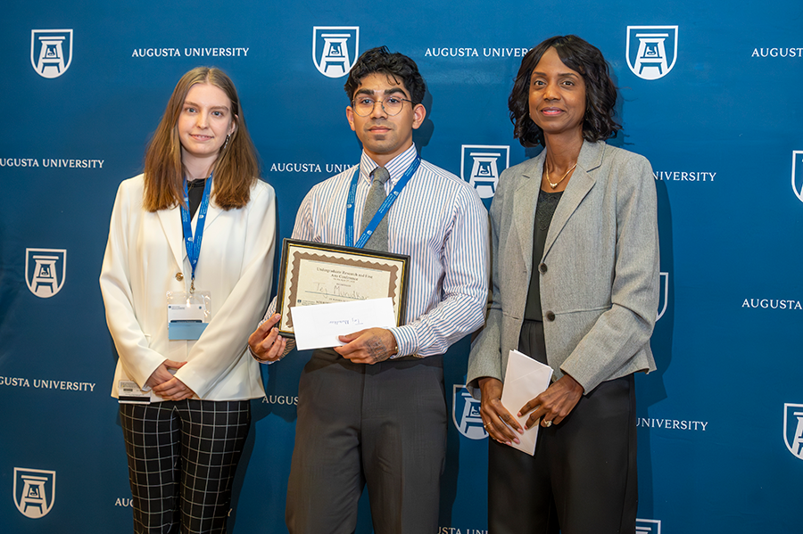 A male college student accepts an award presented by two women.