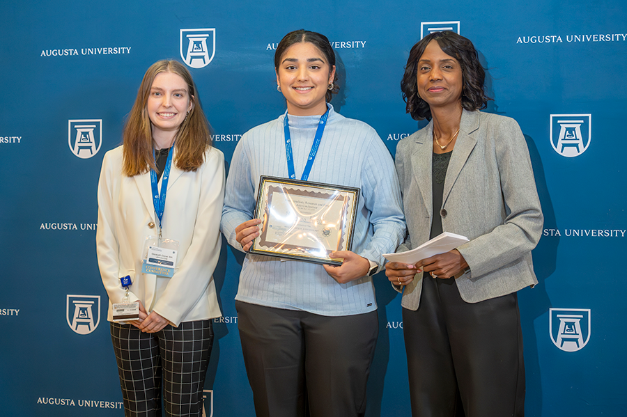 A female college student accepts an award presented by two women.