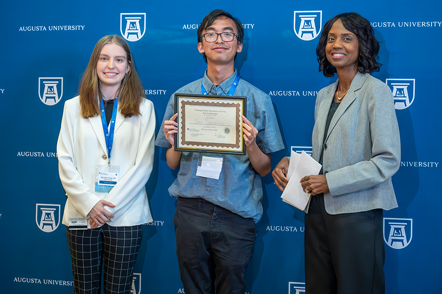 A male college student accepts an award presented by two women.
