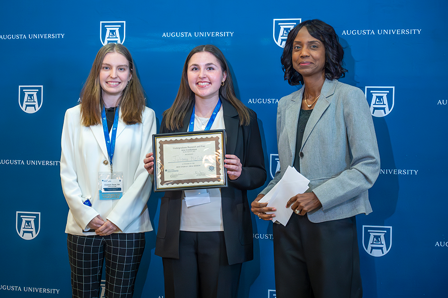 A female college student accepts an award presented by two women.