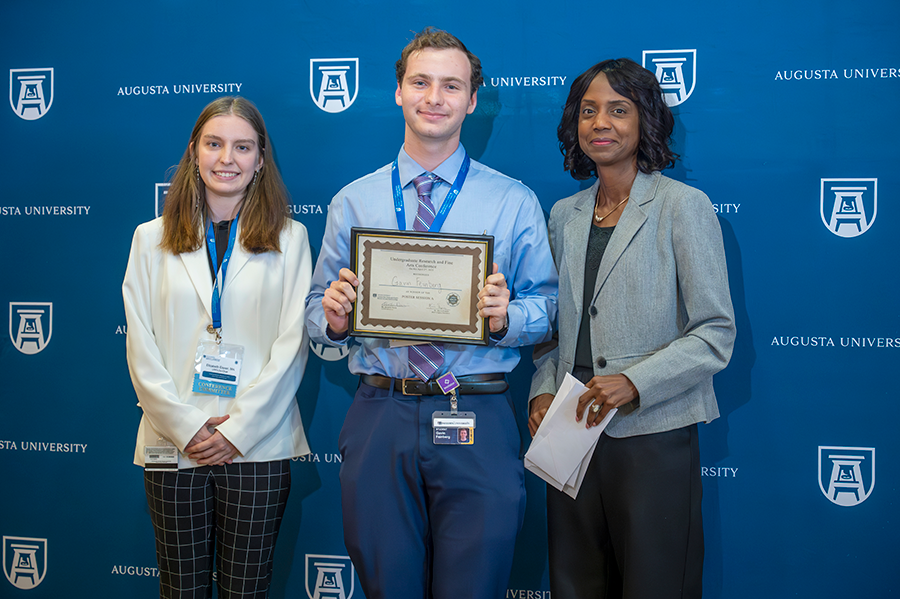 A male college student accepts an award presented by two women.