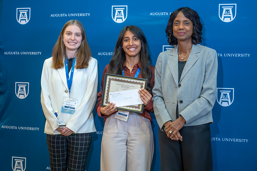 A female college student accepts an award presented by two women.