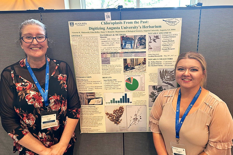 Two women stand next to a scientific poster describing a project they have completed for a competition. Their project is titled, "Chloroplasts From the Past: Digitizing Augusta University's Herbarium."