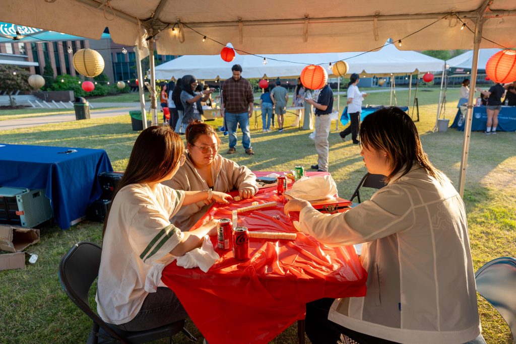 Three college-aged students sit at a table together outdoors.