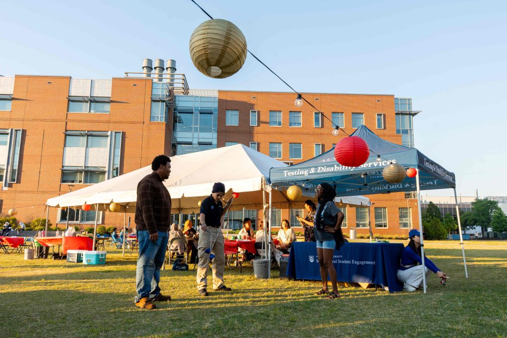 College-aged students attend an outdoor event with string lights and booths.