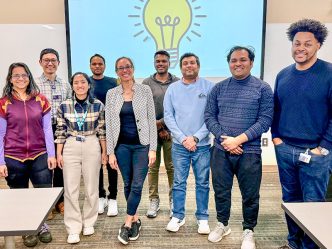 A group of college students and a professor standing in front of display with graphic of lightbulb