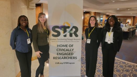Four women standing next to a stand up poster.