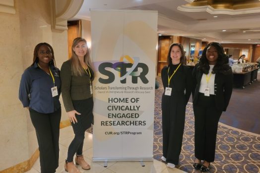 Four women standing next to a stand up poster.