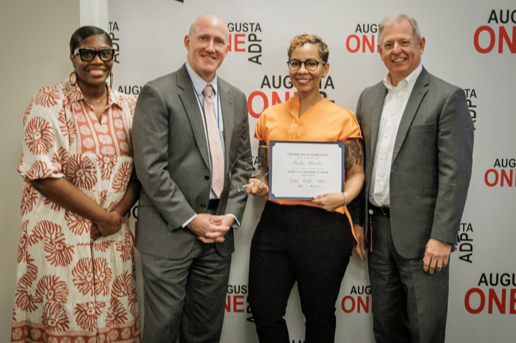 Two men and two women stand in front of an Augusta One ADP banner. The woman second from right holds a certificate.