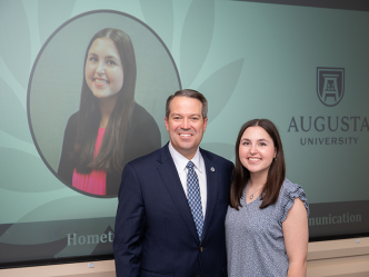 A female college student and a male university president stand during an awards ceremony.