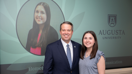 A female college student and a male university president stand during an awards ceremony.