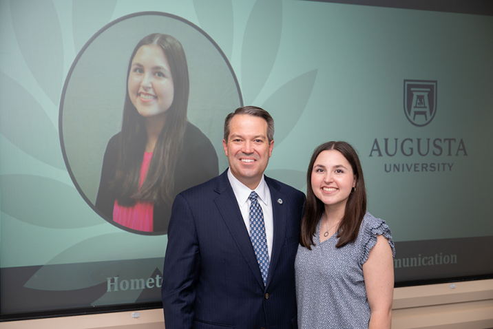 A female college student and a male university president stand during an awards ceremony.