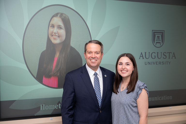 A female college student and a male university president stand during an awards ceremony.
