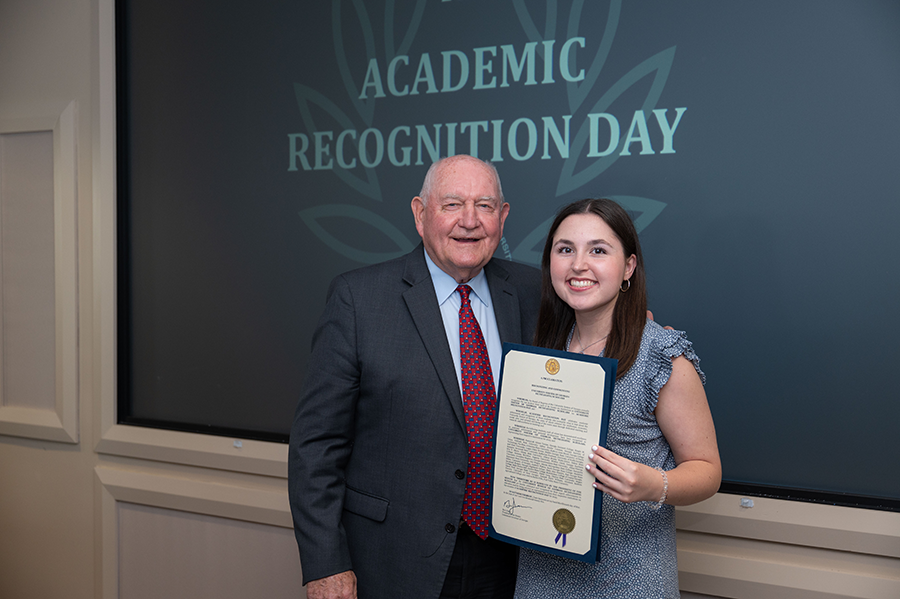 An older man presents a female college student with an award during a special ceremony.