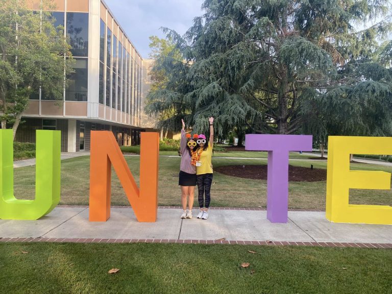 Two women form a capital I between the letters UN and TE to form "Unite" at an outdoor event.