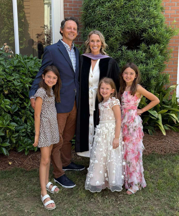 A mother and father and their three little girls pose for a photo at the mother's dental school graduation.
