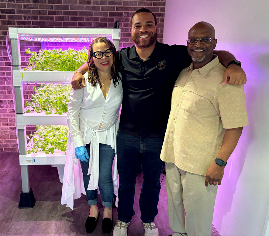 Two men and a woman pose in front of a hydroponic vertical garden.
