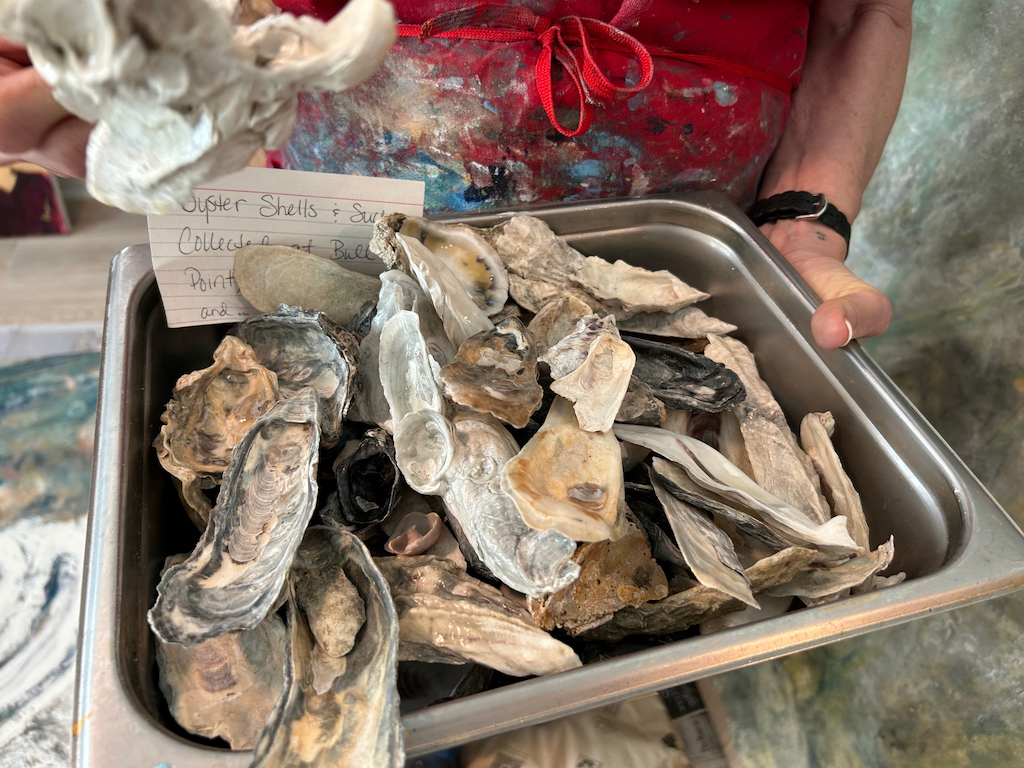A woman holds a tray filled with oyster shells.
