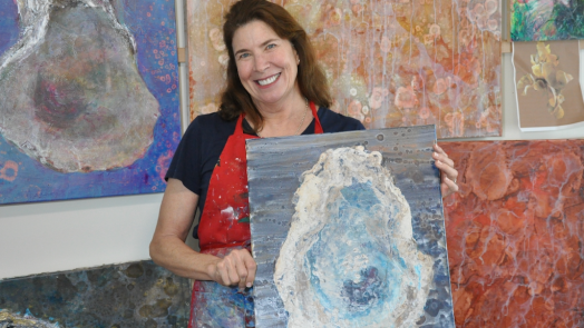 Beth Droppleman, PhD, in a gallery with many of her paintings from the series The Mighty Oyster
