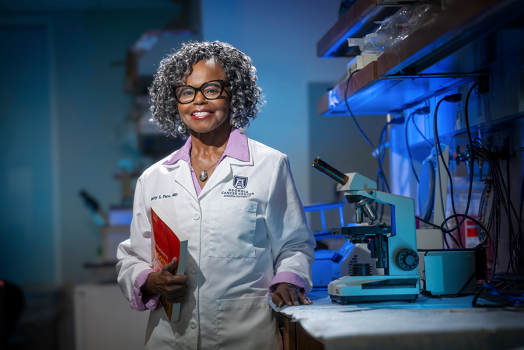 A woman wearing a lab coat stands in a scientific lab.