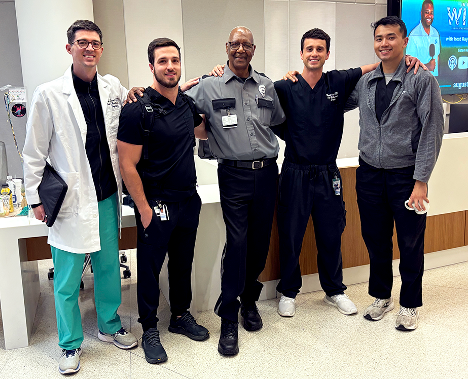 A group of four male medical students pose with Carter in the middle wearing his security officer uniform.