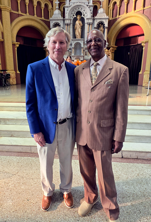 A well-dressed male medical college dean and a security officer pose for a picture in front of a religious dais.