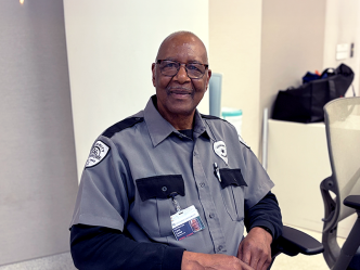 A security guard sits in a chair watching monitors in a large building.