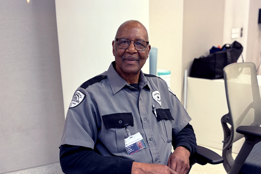 A security guard sits in a chair watching monitors in a large building.