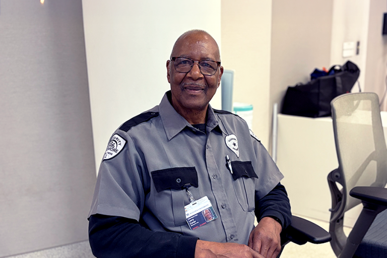 A security guard sits in a chair watching monitors in a large building.