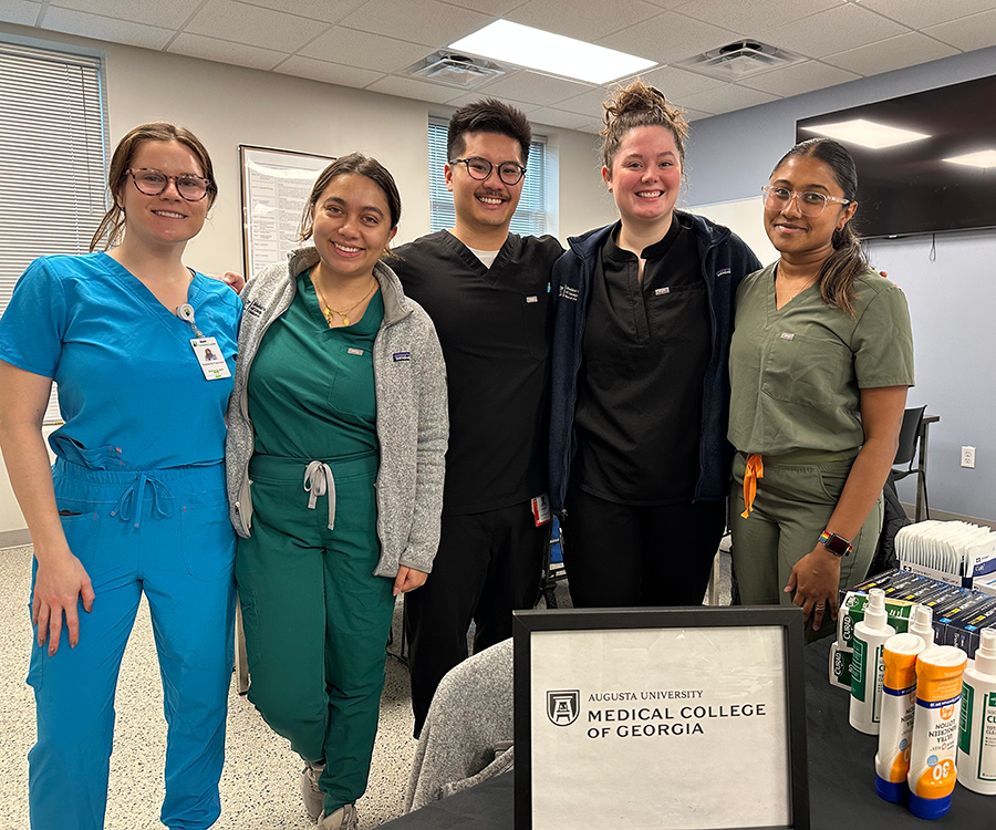 A group of five medical students, four women and one man, stand in a small clinic.