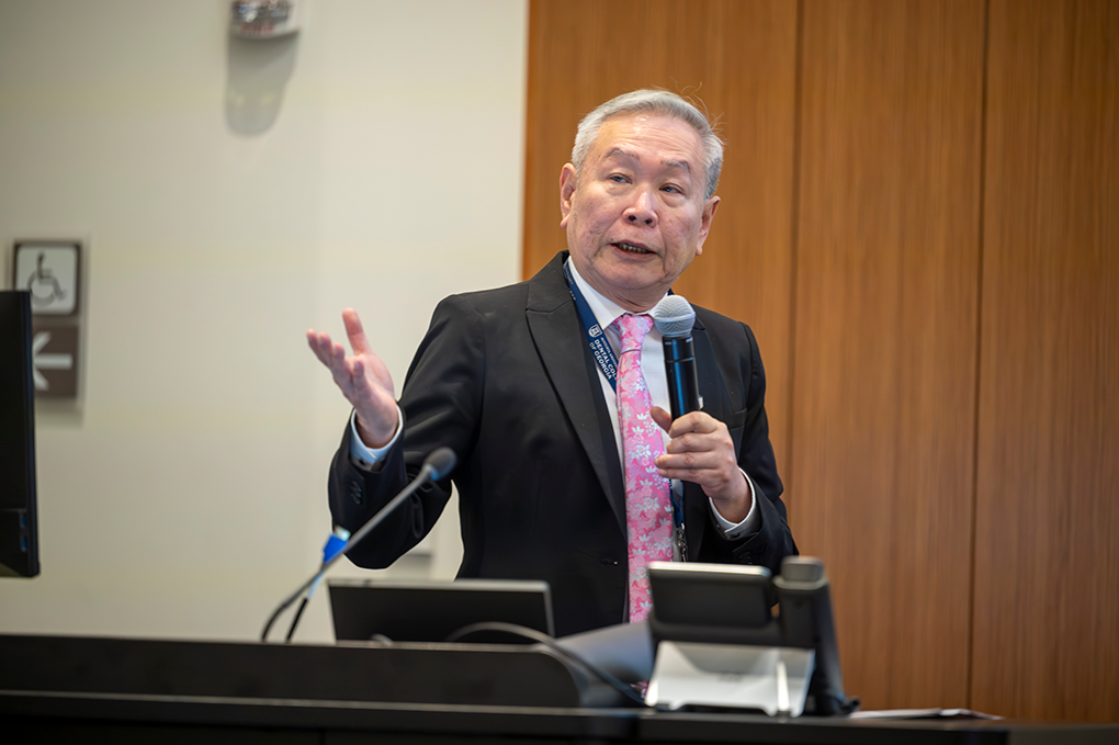 A professionally dressed man holding a microphone speaks at a podium.