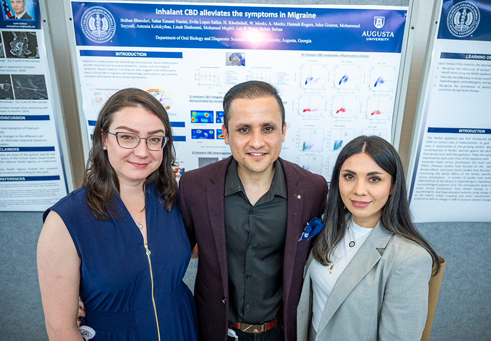 Two women and and a man pose in front of a research project poster about CBD's impacts on migraines.
