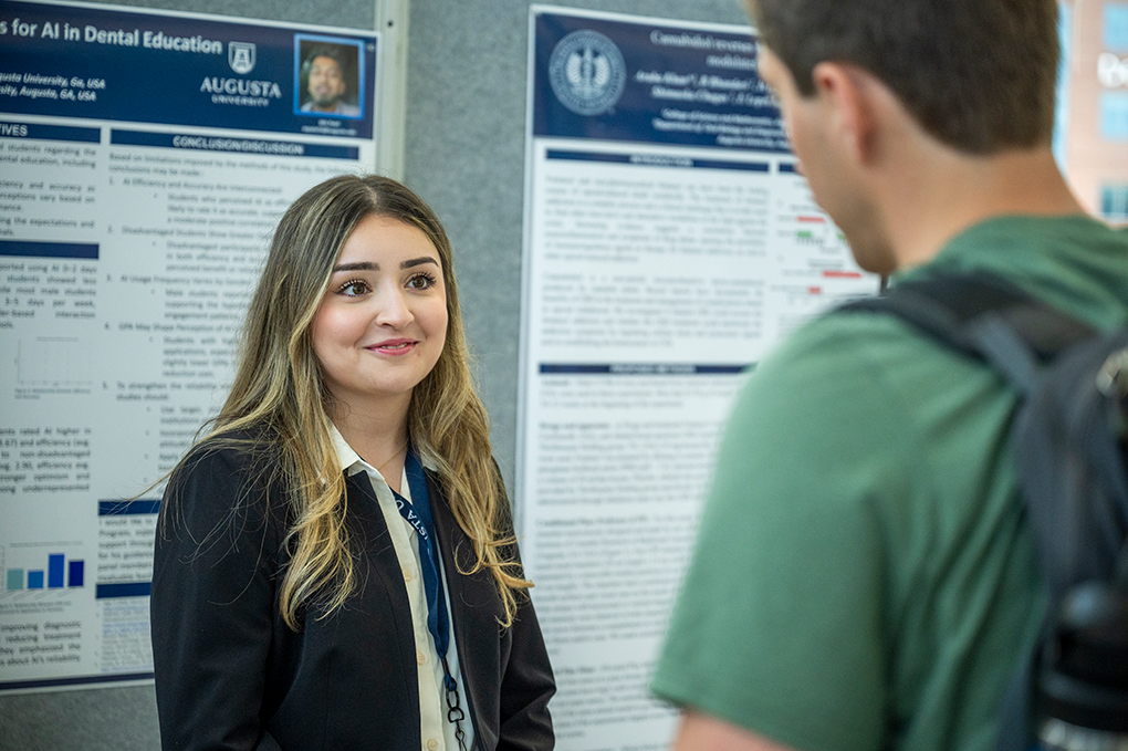 A woman standing in front of a scientific research posters talks to a man.