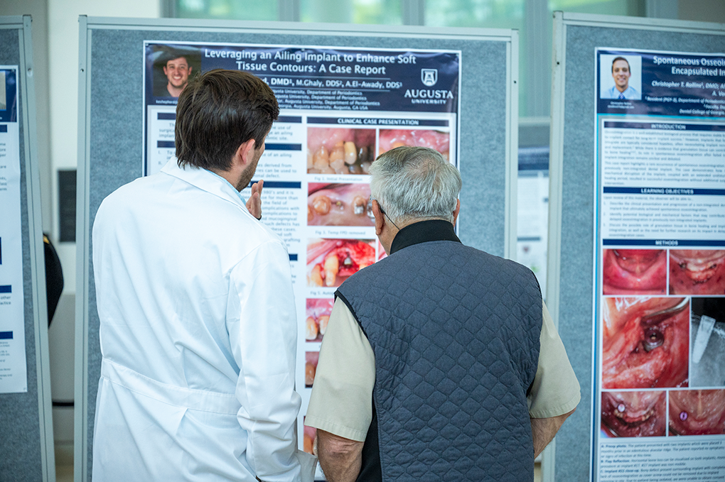 Two men look at a scientific research poster. One is wearing a lab coat.