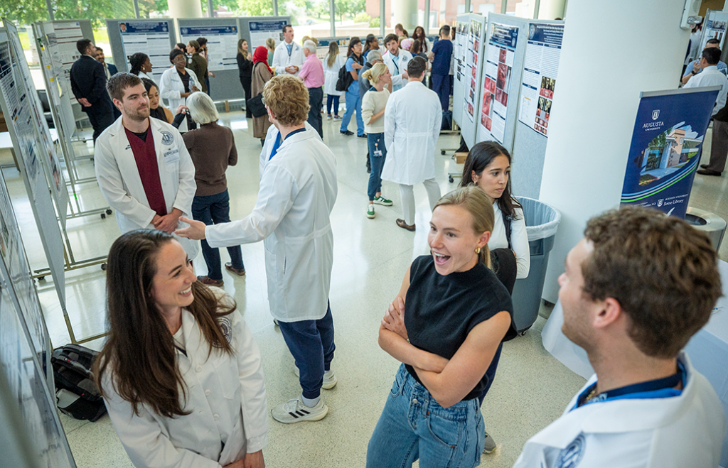 People wearing lab coats and casual clothes chat and look at research poster presentations.