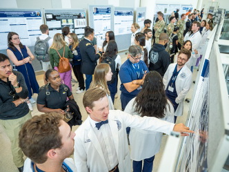 People wearing lab coats and casual clothes chat and look at research poster presentations.
