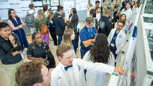 People wearing lab coats and casual clothes chat and look at research poster presentations.