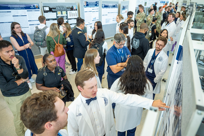 People wearing lab coats and casual clothes chat and look at research poster presentations.